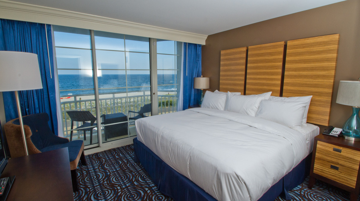 Single king bed in full ocean view wetbar suite with balcony in background