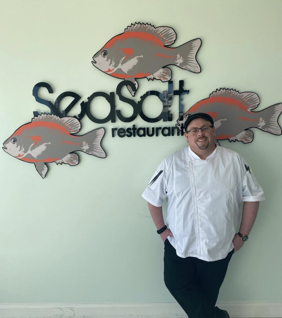 Photo of SeaSalt Restaurant's New Chef, Chef Bowen, standing in front of the SeaSalt Restaurant sign.