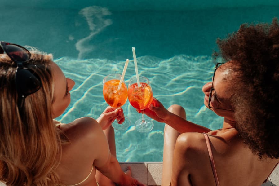 Two guests on vacation sitting poolside and enjoying the drinks they ordered