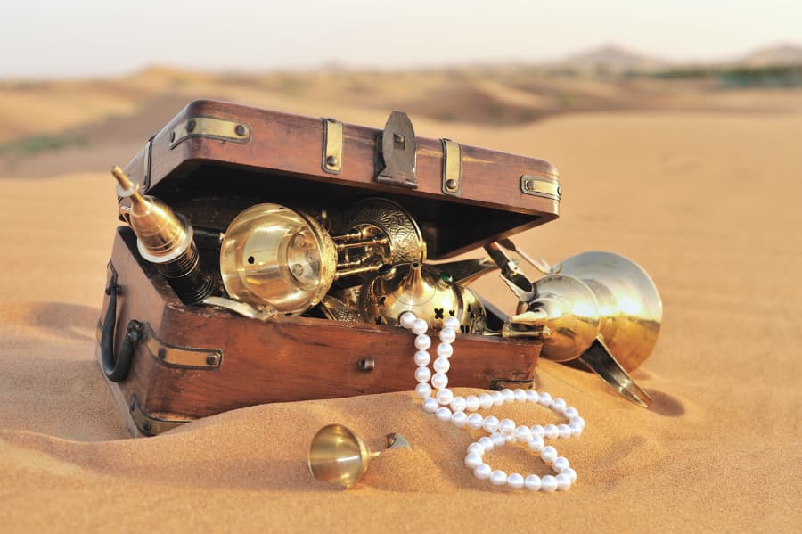 Wooden treasure chest with trinkets lying in sand