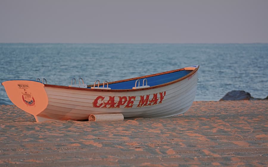 Beachfront with small boat on sand that says Cape May on side