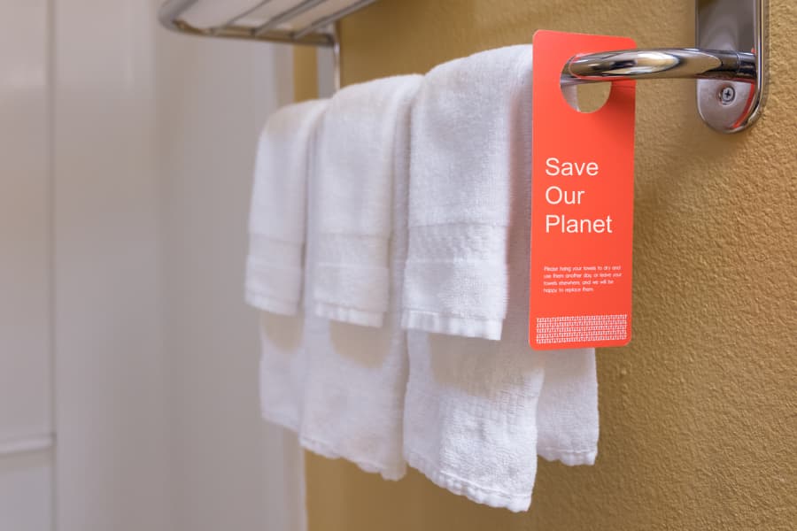 Hotel shower with hanging towels and sign that says save our planet