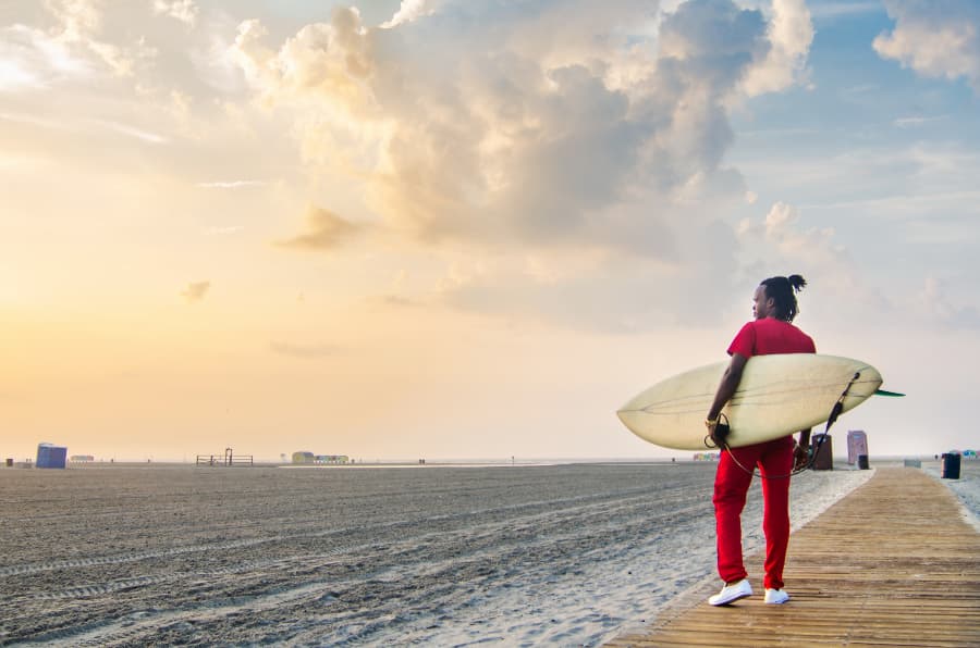 Surfer in red outfit, carrying surf board on boardwalk along beach