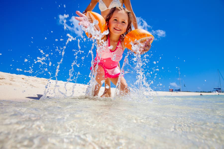 Child in orange floaties splashing in water at beach