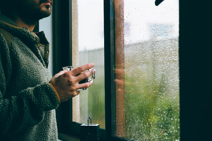 Person holding coffee near window on rainy day