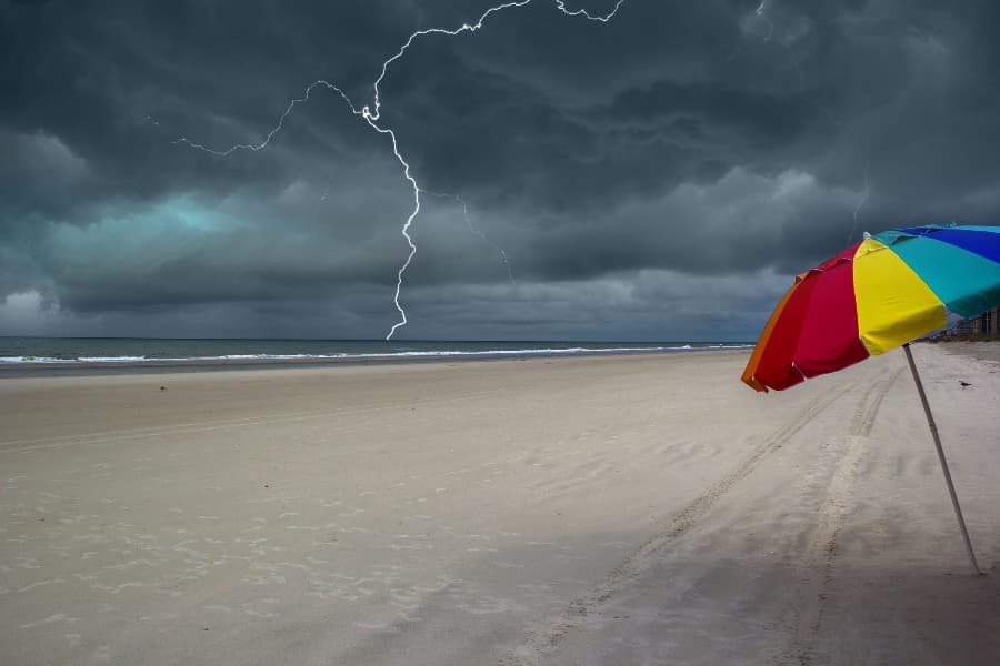 Lightning striking ocean at beach with colorful beach umbrella in sand
