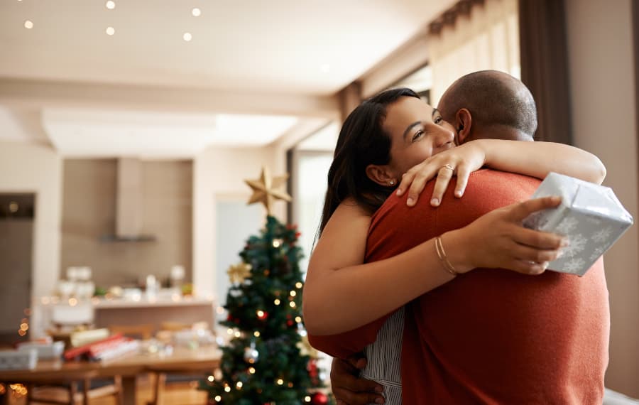 Couple hugging while exchanging holiday gifts at home