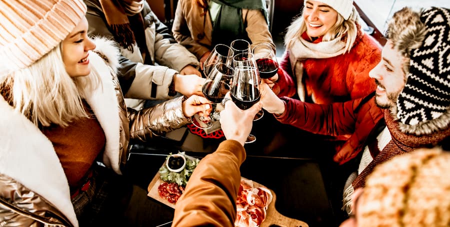 Group of friends toasting red wine at bar restaurant in wintertime during happy hour