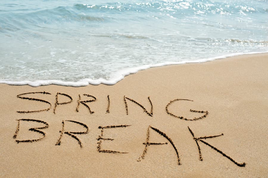 Spring break written in sand on beach with waves in background