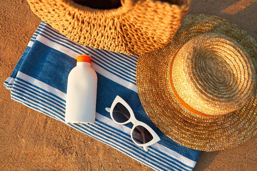 Towel on sand with sunscreen, sunglasses, and straw hat