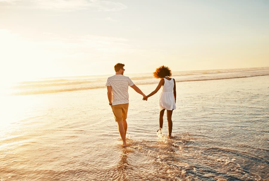couple holding hands while wading in water at beach