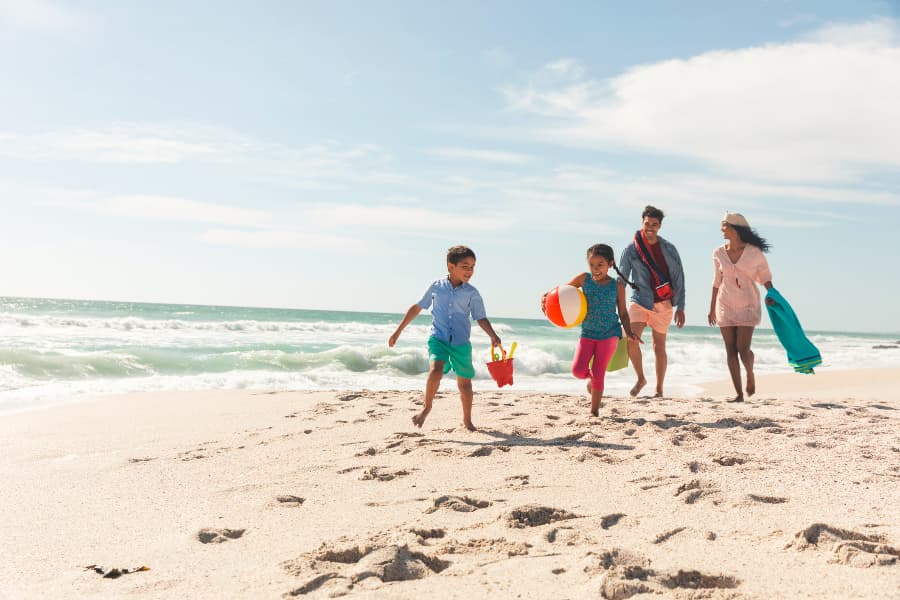 Family playing together on beach with towel, ball, and sand pail