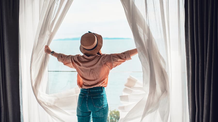 Woman opening white curtains to reveal ocean views